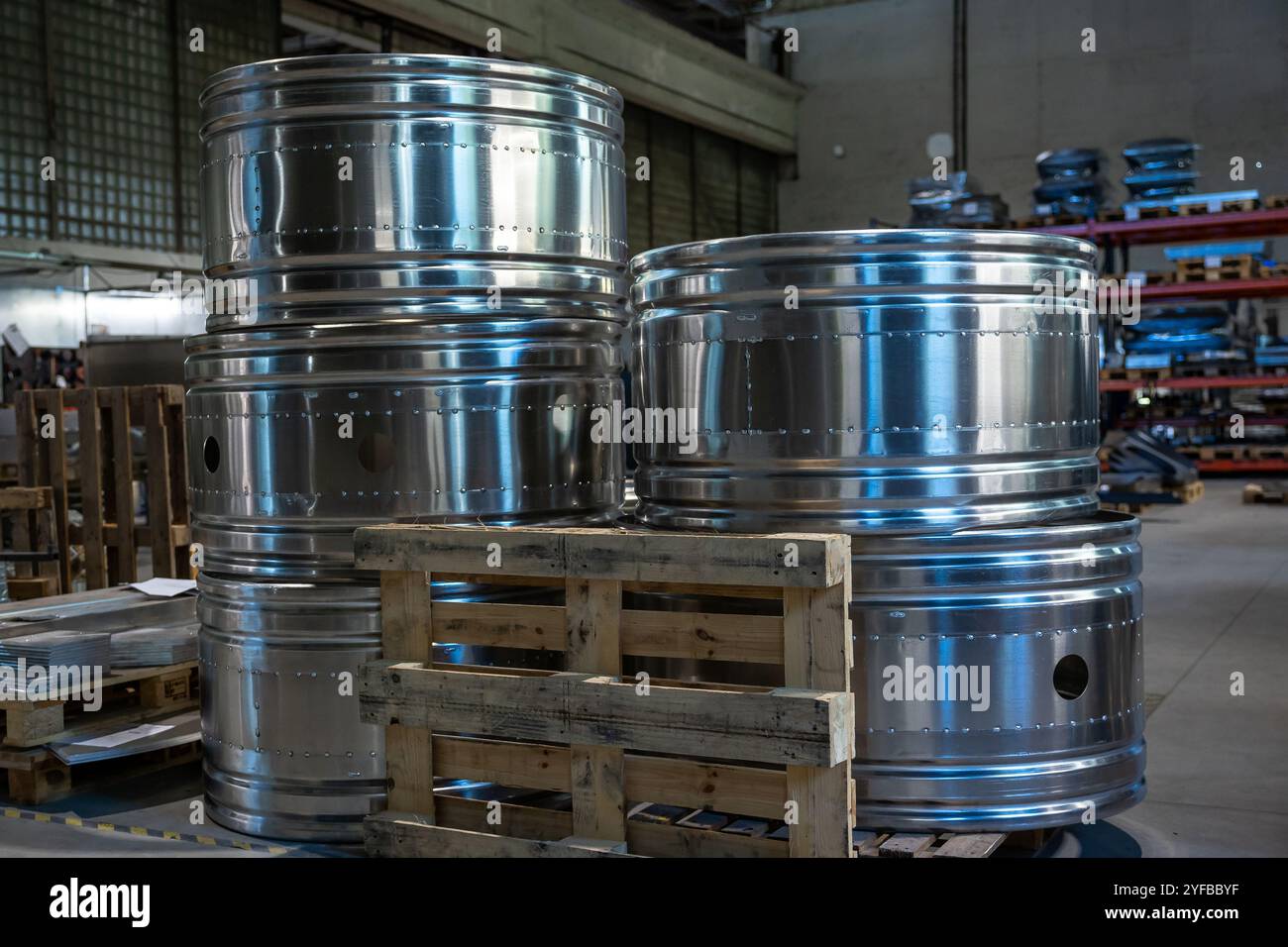 Nahaufnahme großer Metallzylinder auf Holzpaletten in einer Fabrik, die ihre polierte Oberfläche und ihre industrielle Umgebung betonen. Stockfoto