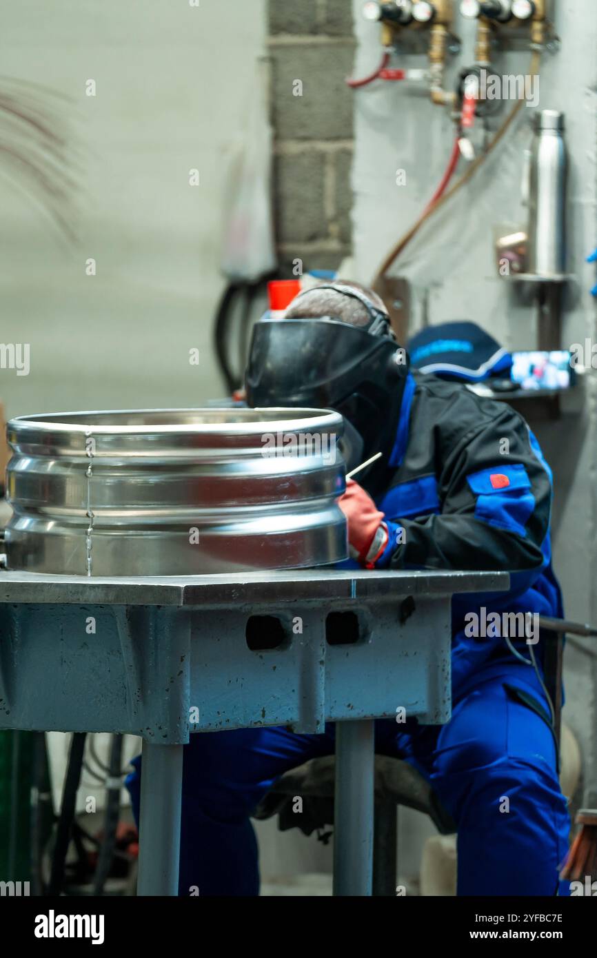 Ein Schweißer, der auf einer Werkbank sitzt und einen großen Metallring schweißt, demonstriert Präzision und Liebe zum Detail in der Werkstatt. Stockfoto