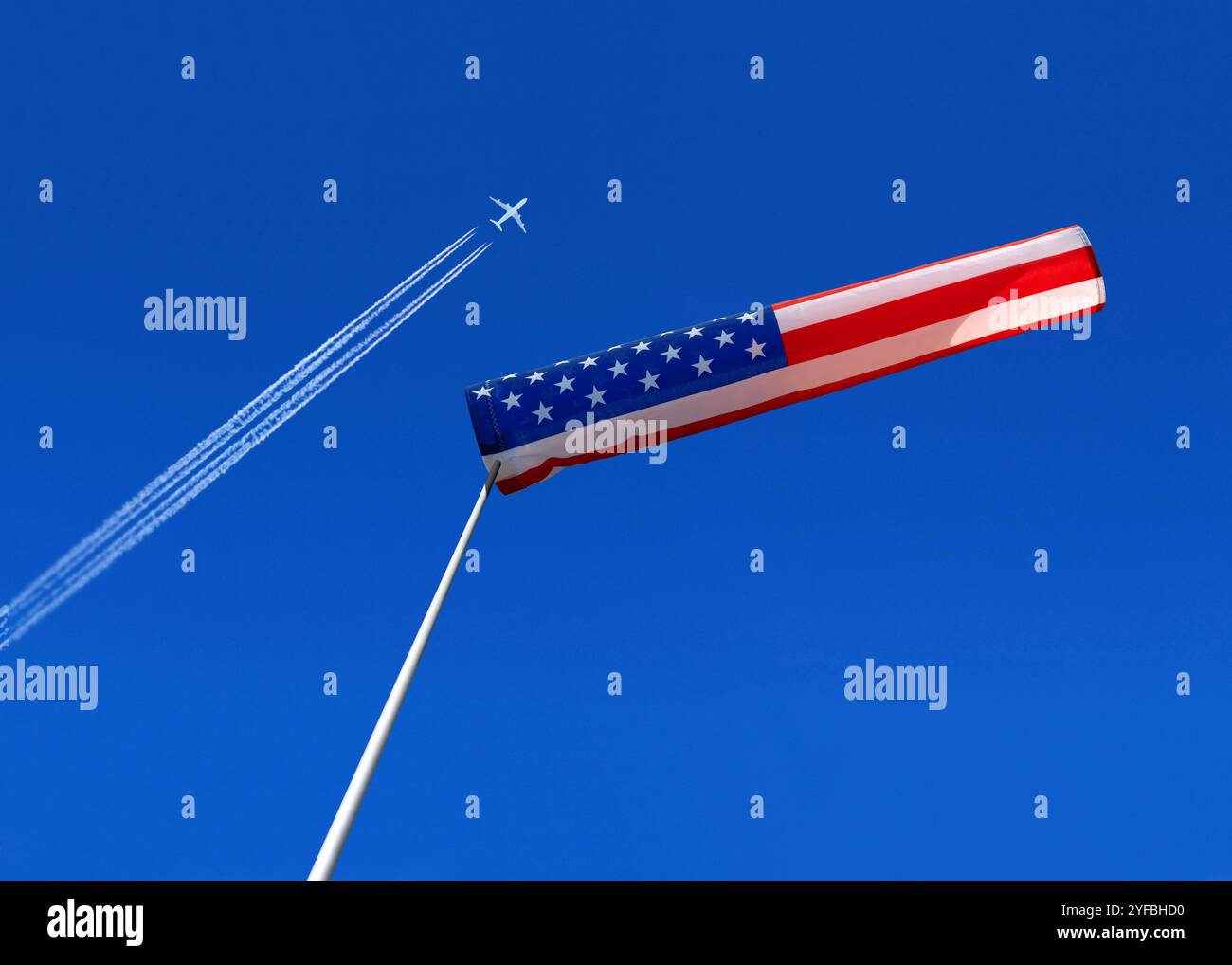 Windsocke bei starkem Wind in den Farben der Nationalflagge der USA vor blauem Himmel mit einem Passagierflugzeug mit Kondensstreifen Stockfoto