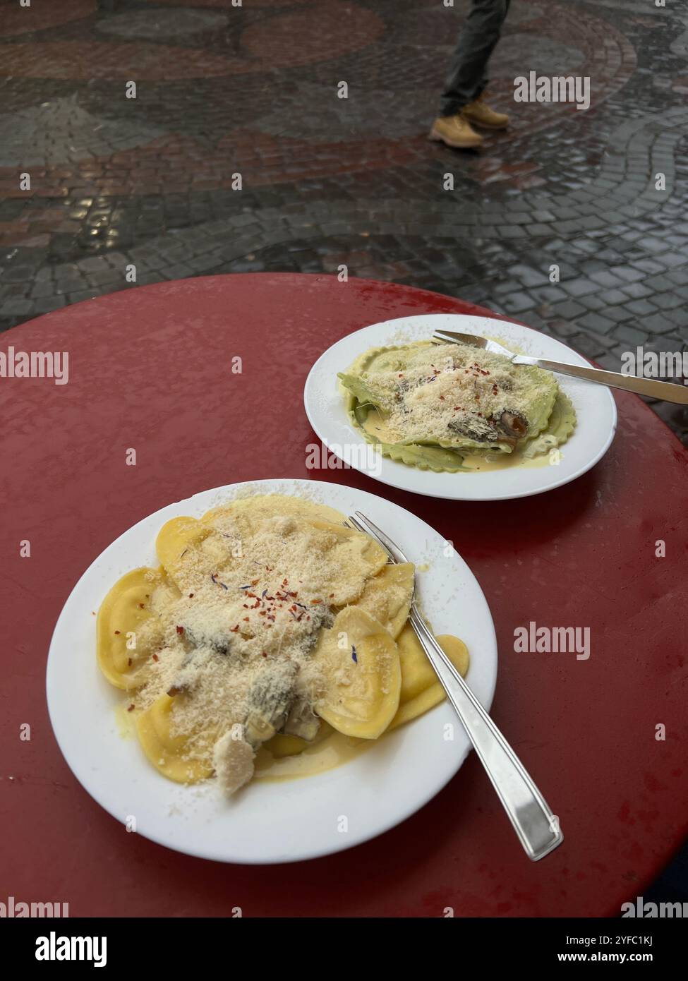 Zwei Teller köstlicher Ravioli auf einem roten Tisch im Freien in regnerischer Umgebung, wahrscheinlich in einer Kopfsteinpflasterstraße in Basel, Schweiz - Smartphone-aufgenommenes Stockfoto