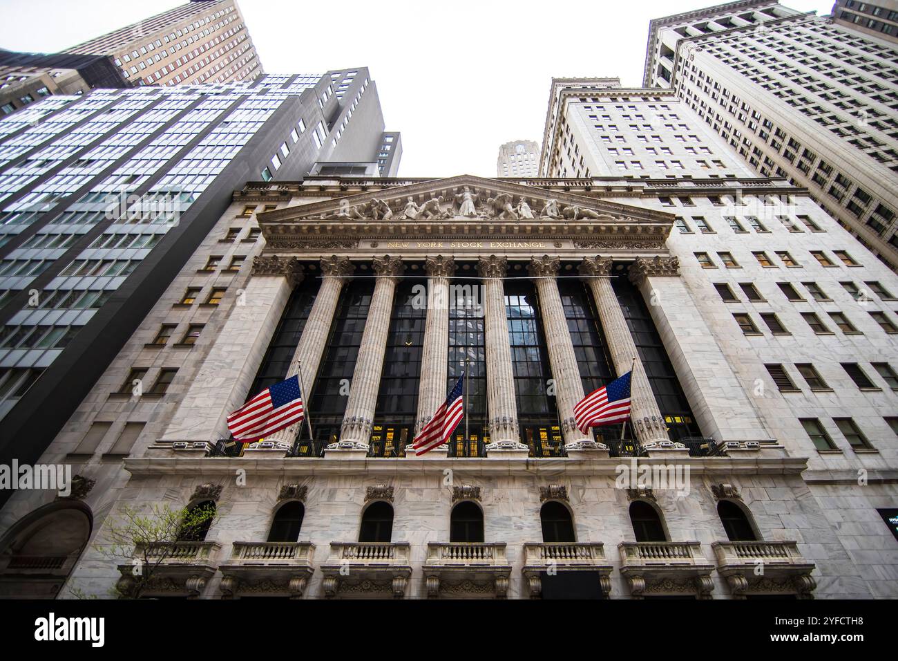 Die Fassade des New York Stock Exchange Gebäudes mit amerikanischen Flaggen, umgeben von hohen Wolkenkratzern. Stockfoto