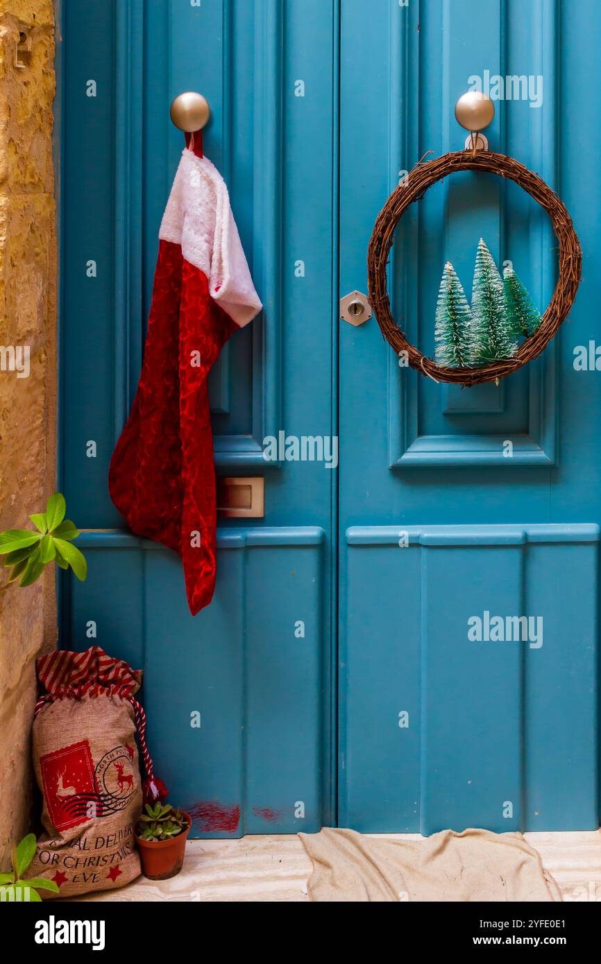 Eine bezaubernde blaue Tür mit Weihnachtsstrumpf und -Kranz, die Weihnachtsstimmung und festliche Stimmung weckt. Perfekt zur Illustration von Weihnachtsthemen a Stockfoto