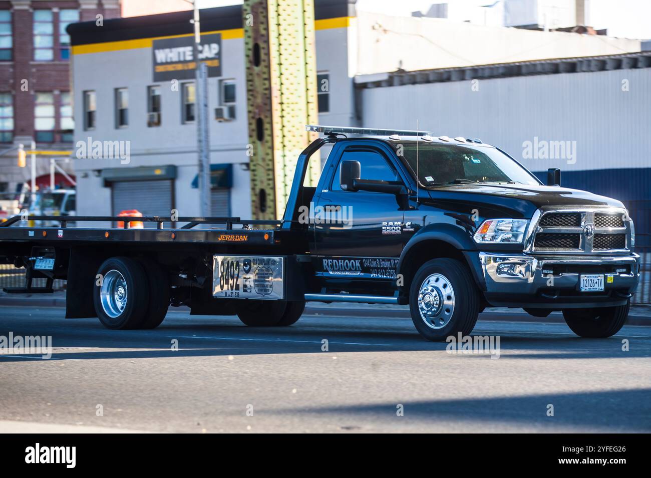 Schwarzer Abschleppwagen, der auf einer Stadtstraße in der Nähe von Industriegebäuden fährt. Stockfoto