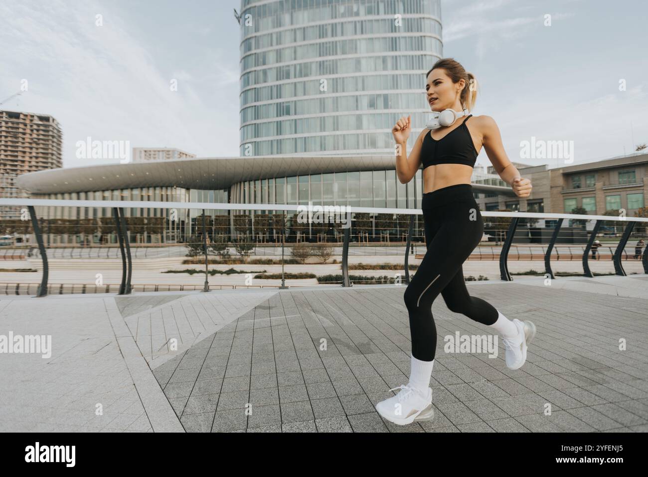 Beim Joggen auf einem stilvollen urbanen Fußweg genießt eine Frau die erfrischende Luft im Freien, umgeben von zeitgenössischer Architektur und einer ruhigen Atmosphäre Stockfoto