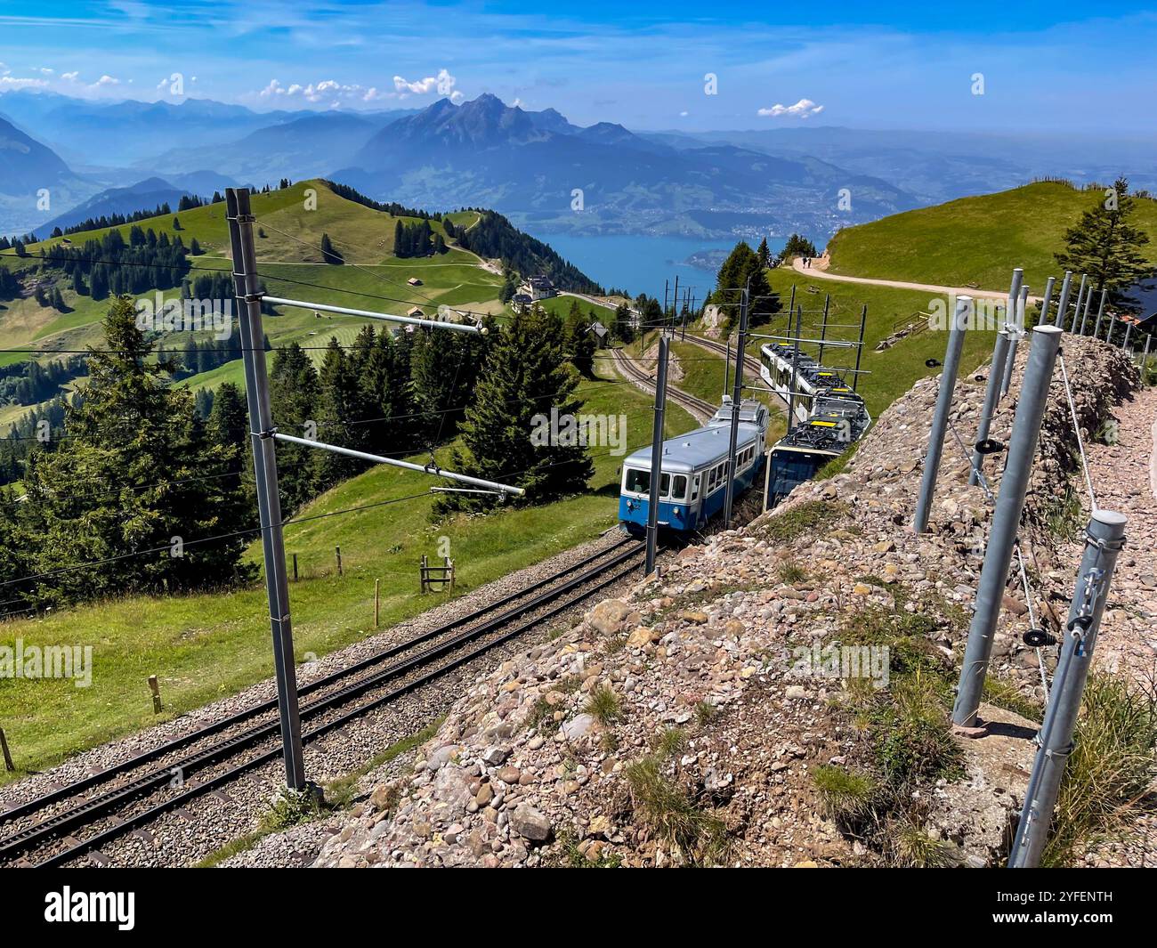 Blaue Züge der Rigi Railways, die den Berg in idyllischer Sommerlandschaft mit See und Bergkette im Hintergrund aufwärts fahren, Rigi Kulm, Schweiz Stockfoto