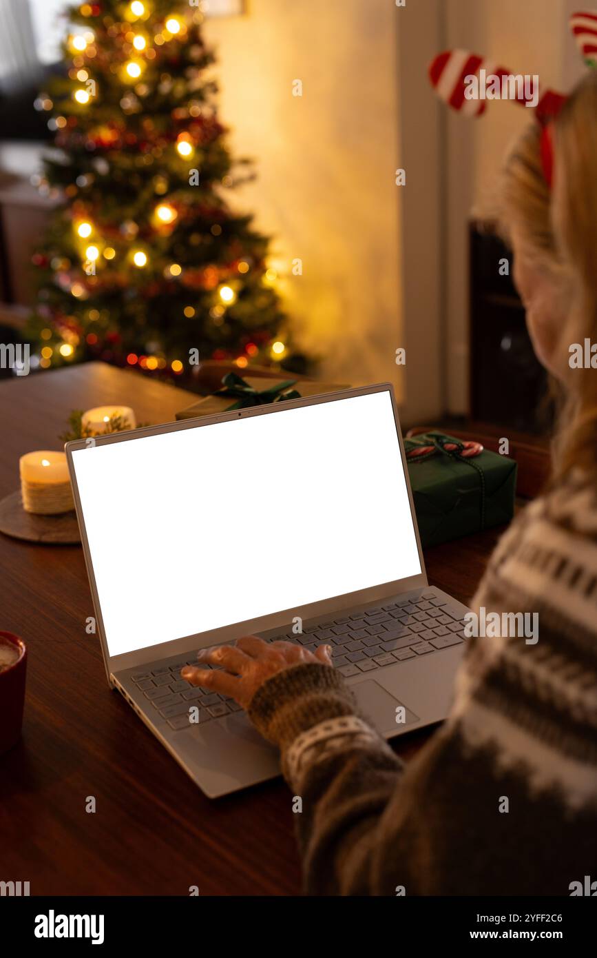 Ältere Frau, die zu Hause den Laptop benutzt, Weihnachtsbaum im Hintergrund glüht, Kopierraum Stockfoto