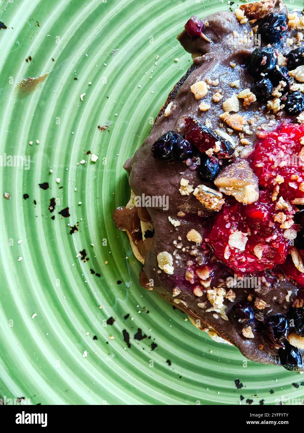 Dekadenter Schokoladenpfannkuchen mit Haselnüssen, Brombeeren und Himbeeren auf grüner Platte – Dessert-Genuss. Stockfoto
