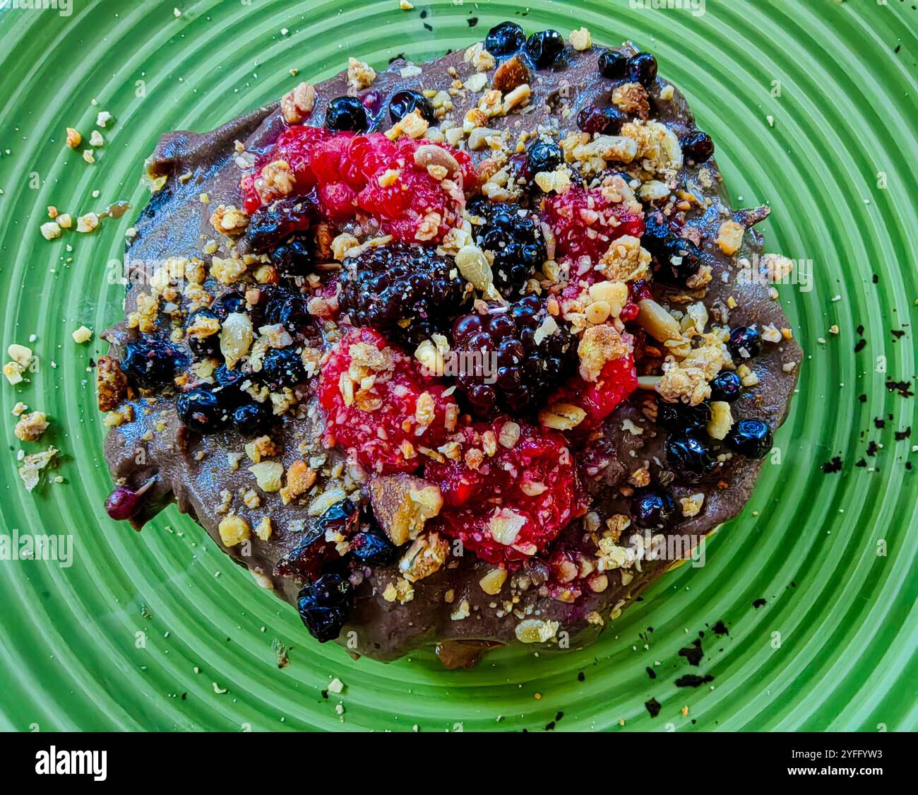 Dekadenter Schokoladenpfannkuchen mit Haselnüssen, Brombeeren und Himbeeren auf grüner Platte – Dessert-Genuss. Stockfoto