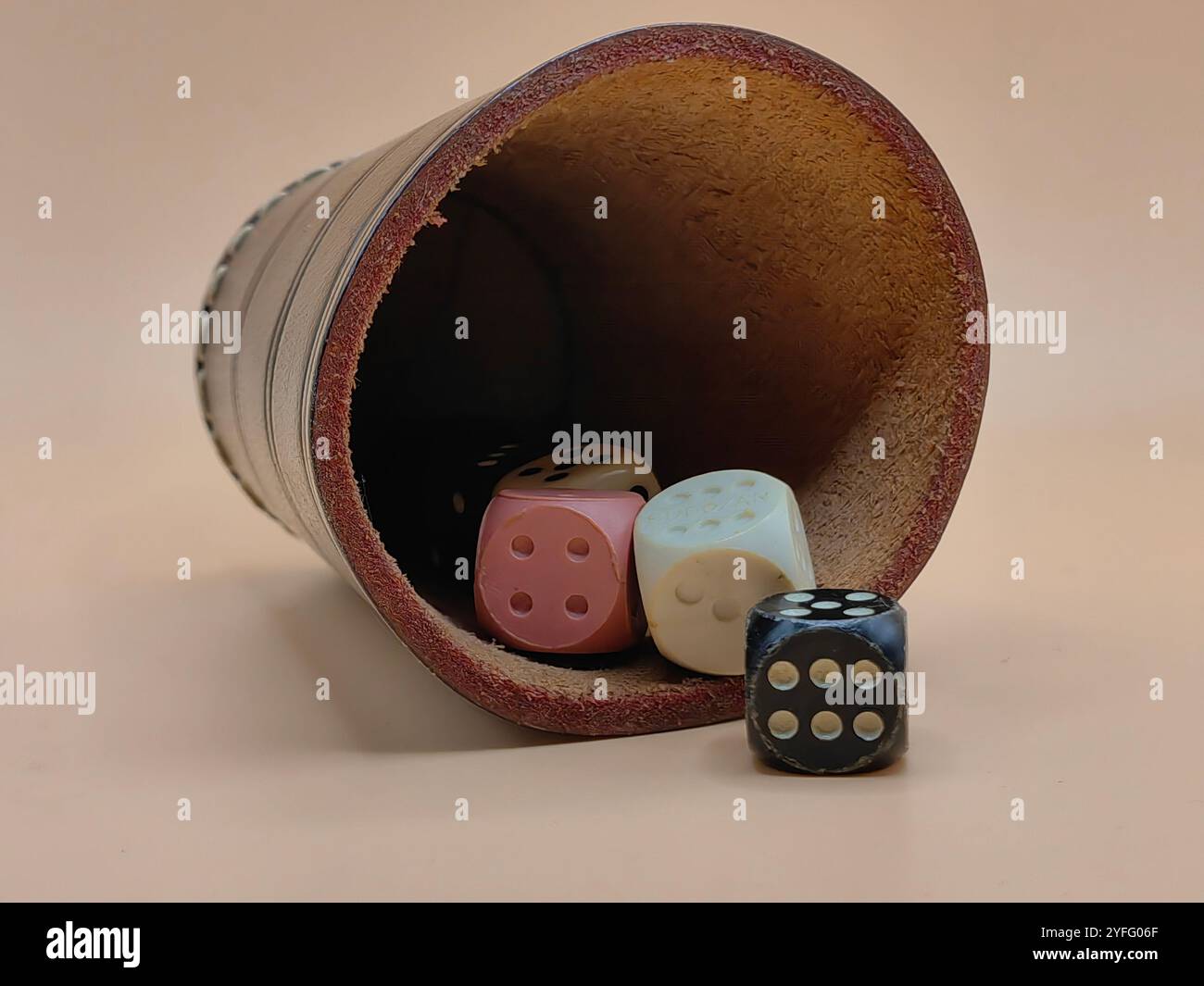 Shake and Roll the Dice – Lederwürfelbecher mit bunten Würfeln auf hellbraunem Hintergrund Stockfoto