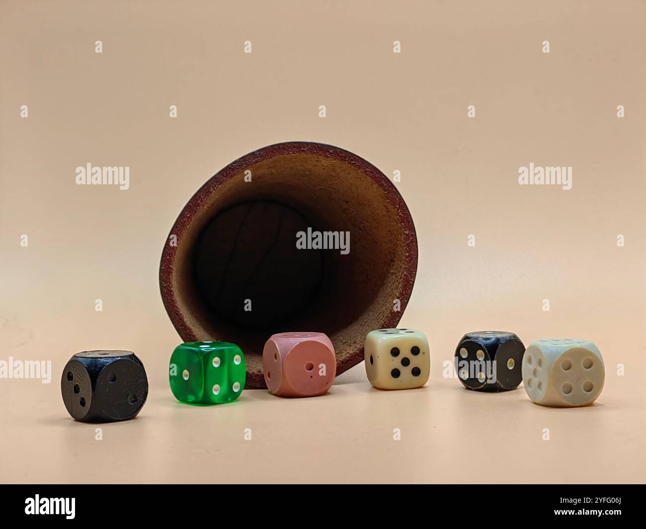 Shake and Roll the Dice – Lederwürfelbecher mit bunten Würfeln auf hellbraunem Hintergrund Stockfoto