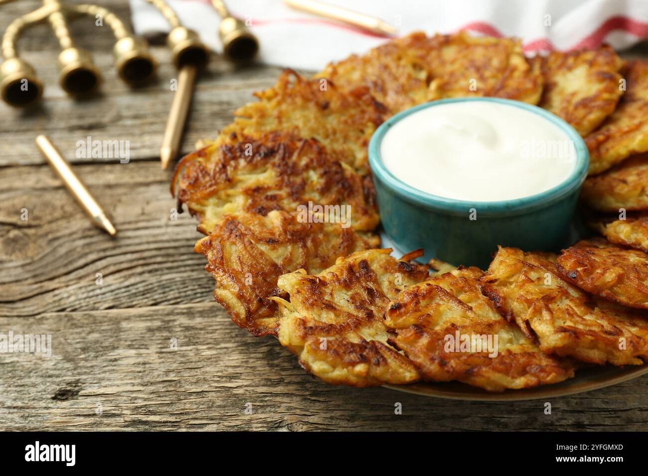 Leckere Kartoffelpfannkuchen, Sauerrahm, Menora und Kerzen auf Holztisch, Nahaufnahme. Hanukkah festliches Essen Stockfoto