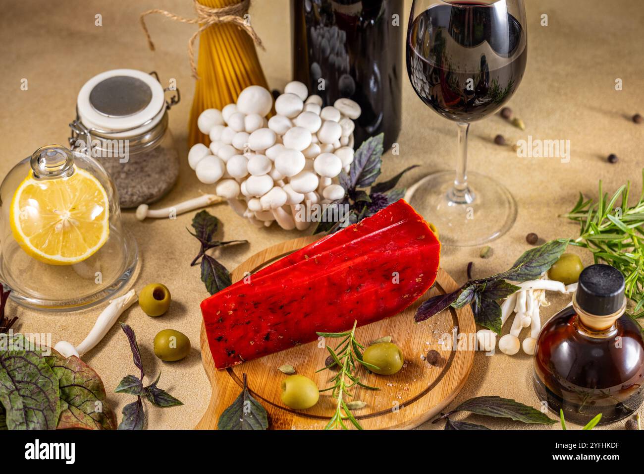 Roter Pesto-Käse auf Holzbrett, umgeben von frischen Zutaten, Wein und Balsamico-Essig, schafft eine einladende Szene für Liebhaber der italienischen Küche Stockfoto