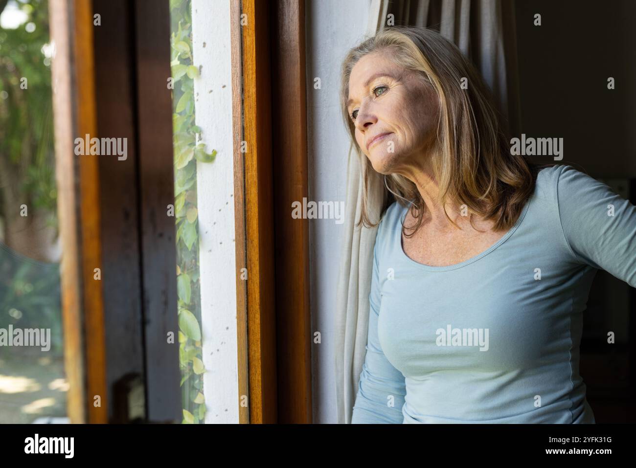 Sie blickt aus dem Fenster, die Seniorin reflektiert friedlich zu Hause, verloren in Gedanken Stockfoto