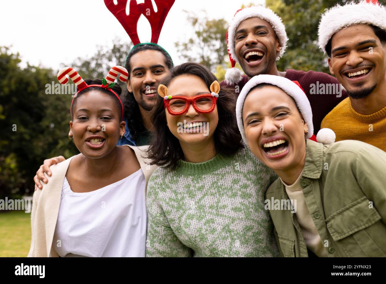 Festliche Hüte tragen, multirassische Freunde feiern Weihnachten im Freien, lachen fröhlich zusammen Stockfoto