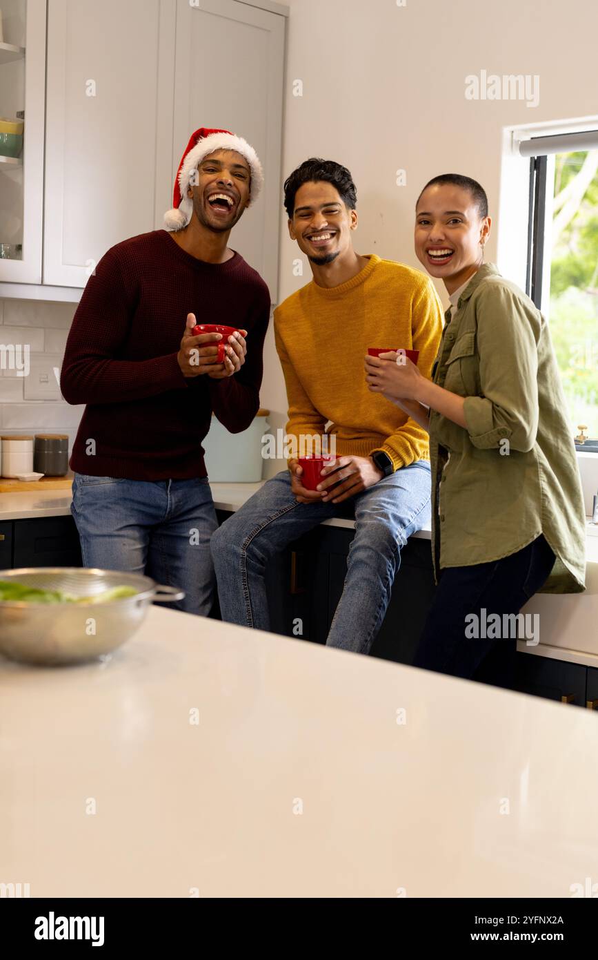 Multirassische Freunde lachen und genießen heiße Getränke während der weihnachtsfeier zu Hause Stockfoto