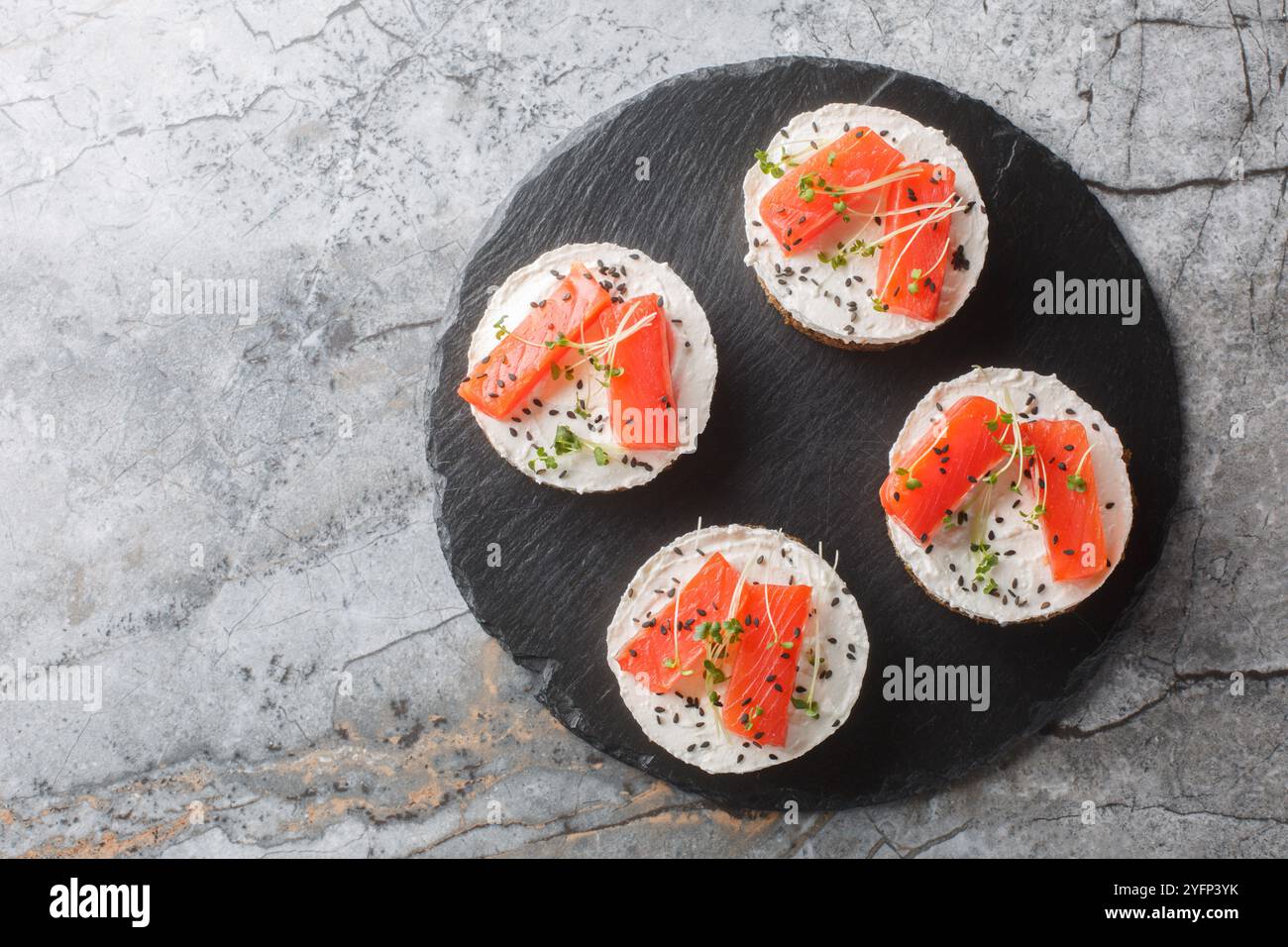 Mini-Käsekuchen-Lachs mit Frischkäse, Sesam und Mikrogemüse, Nahaufnahme auf Schieferplatte auf dem Tisch. Horizontale Draufsicht von oben Stockfoto