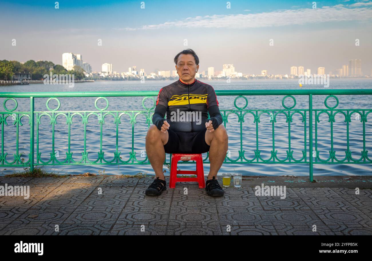 Ein vietnamesischer Mann mittleren Alters in Fahrradkleidung ruht an einem Sonntagmorgen neben dem Westsee in Hanoi, Vietnam. Stockfoto