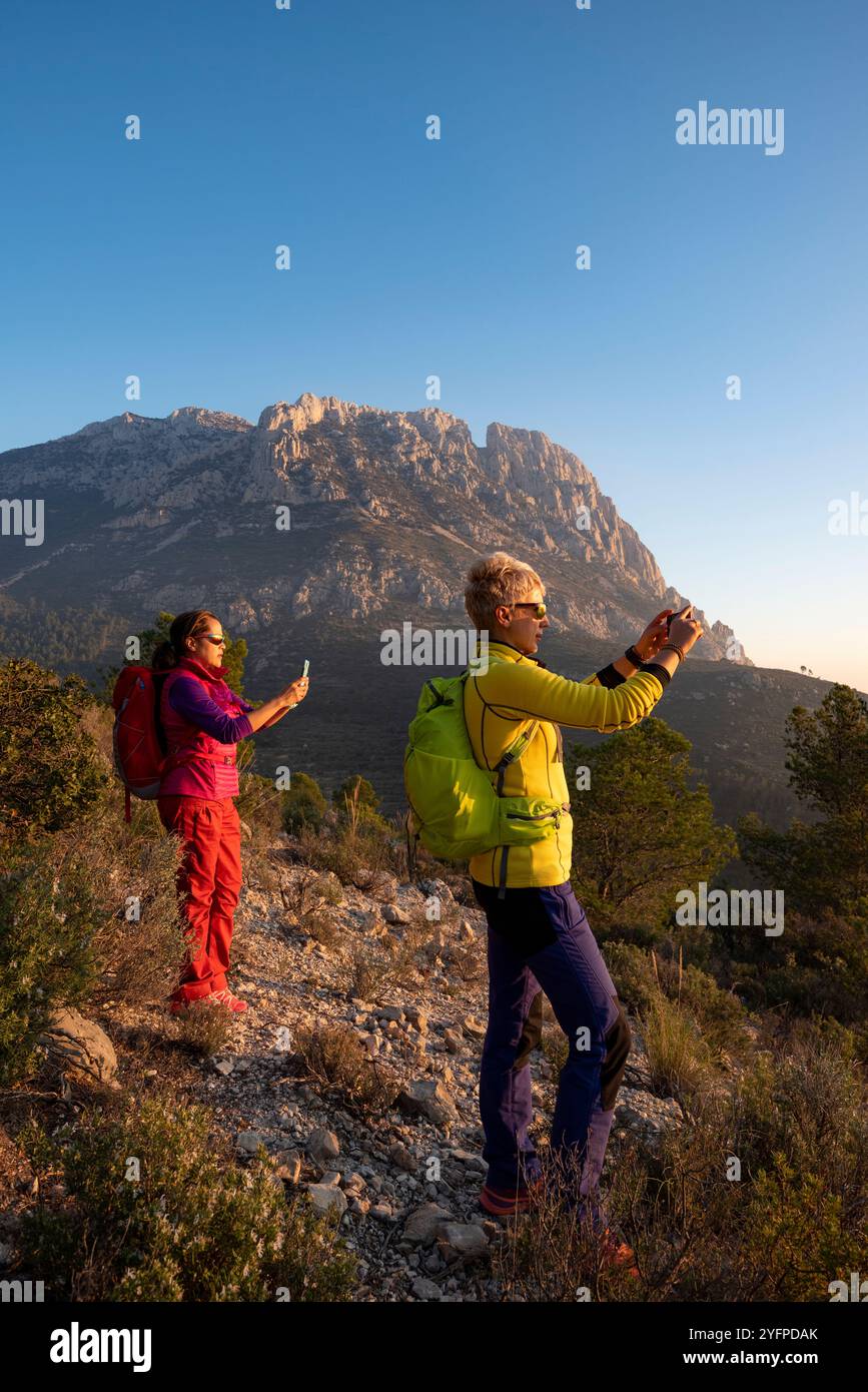 Zwei junge Frauen wandern in den Bergen und machen Fotos bei Sonnenuntergang, Sella-Tal, Provinz Alicante, Spanien - Stockfoto Stockfoto
