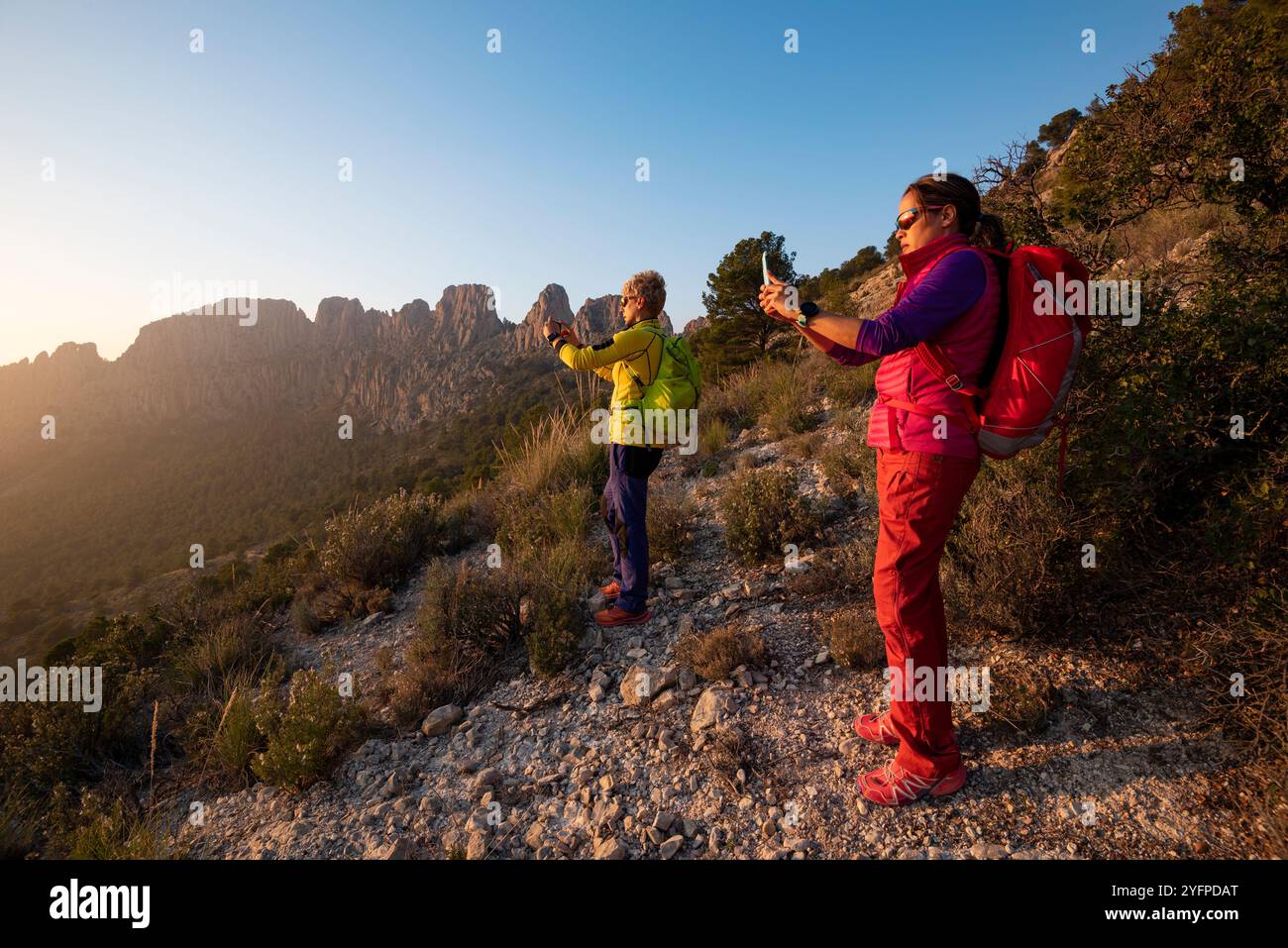 Zwei junge Frauen wandern in den Bergen und machen Fotos bei Sonnenuntergang, Sella-Tal, Provinz Alicante, Spanien - Stockfoto Stockfoto