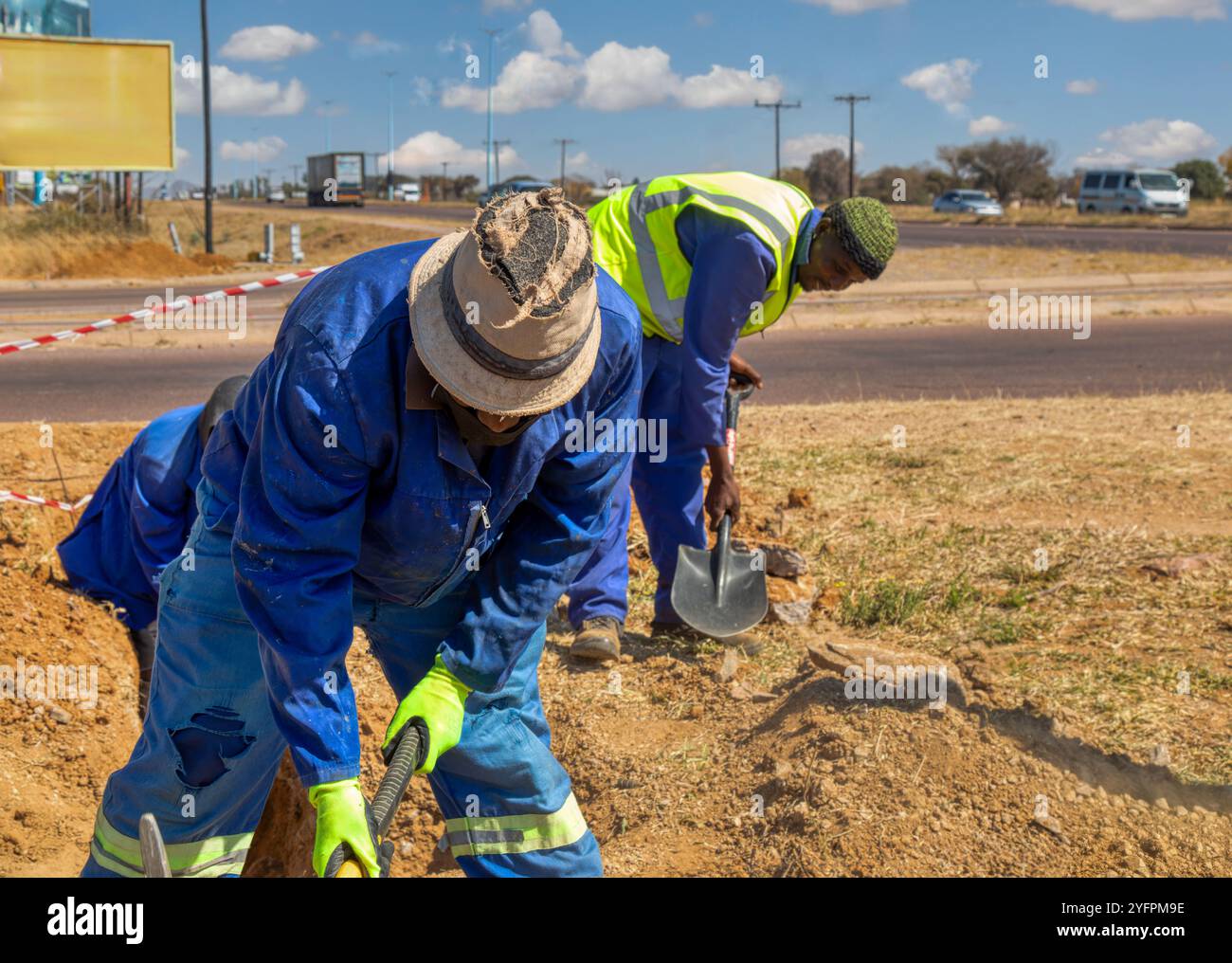 Zwei afrikanische Arbeiter graben einen Graben an der Seite der Autobahn und installieren Glasfaser für Telekommunikationsunternehmen Stockfoto Zwei afrikanische Arbeiter graben einen Graben an der Seite der Autobahn und installieren Glasfaser für Telekommunikationsunternehmen Stockfoto