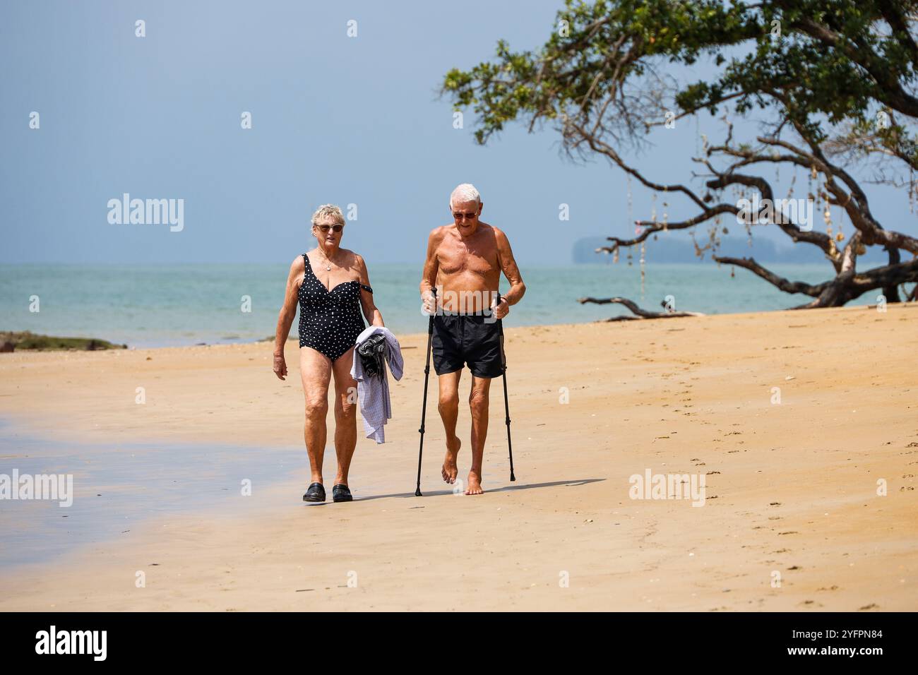 Älteres Paar, das am Sand auf dem Meeresgrund spaziert. Frau und Mann mit Stöcken an einem tropischen Strand, Leben im Ruhestand Stockfoto