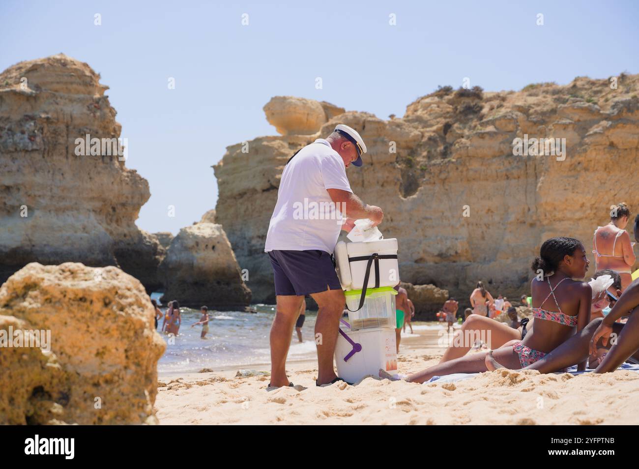 Ein freundlicher Verkäufer verkauft eine traditionelle Bola de Berlim an einen Strandgänger im Praia de São Rafael, eingerahmt von den Klippen der Algarve Stockfoto