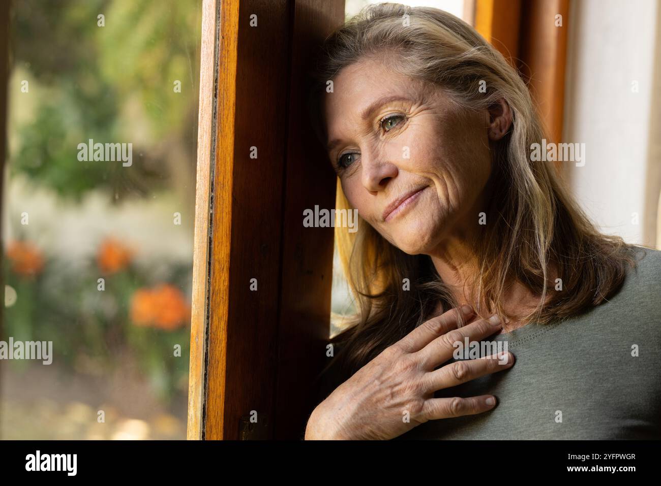 Eine nachdenkliche Seniorin blickt aus dem Fenster und genießt einen friedlichen Moment zu Hause Stockfoto