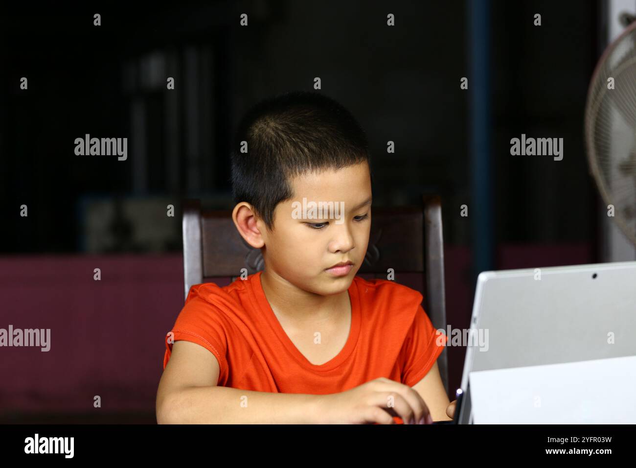 Ein zielgerichtetes Kind beschäftigt sich zu Hause mit der Technik, indem es an einem Notebook arbeitet. Die Szene fängt das Wesen des modernen Lernens und der Neugier der Jugend ein. Stockfoto