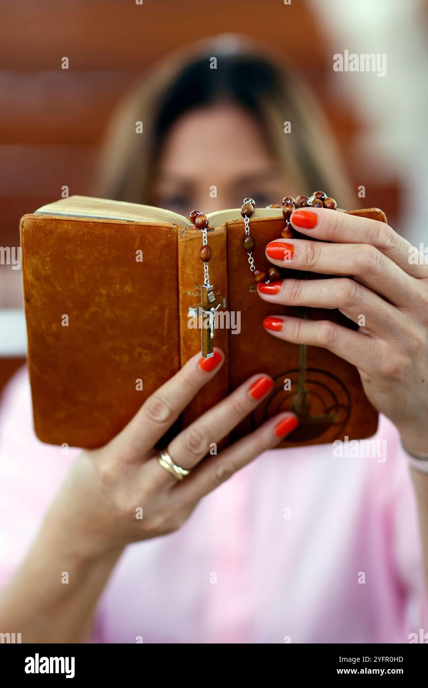 Eine Frau liest eine alte Bibel mit Rosenkranz in einer Kirche. Stockfoto