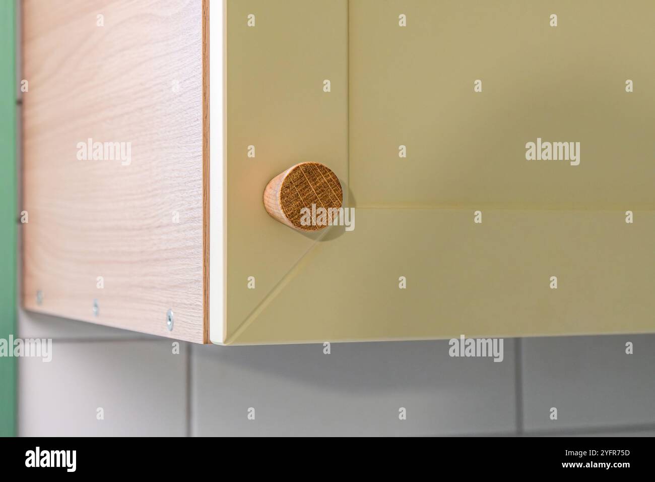 Holzgriff am gelben, schlanken Küchenschrank mit schlichtem Design befestigt. Schrankknopf aus massiver Eiche aus nächster Nähe Stockfoto