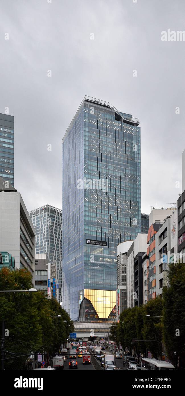 Moderner Glashochhaus in einem belebten Stadtgebiet, umgeben von Geschäften und Fußgängern an einem bewölkten Tag Stockfoto