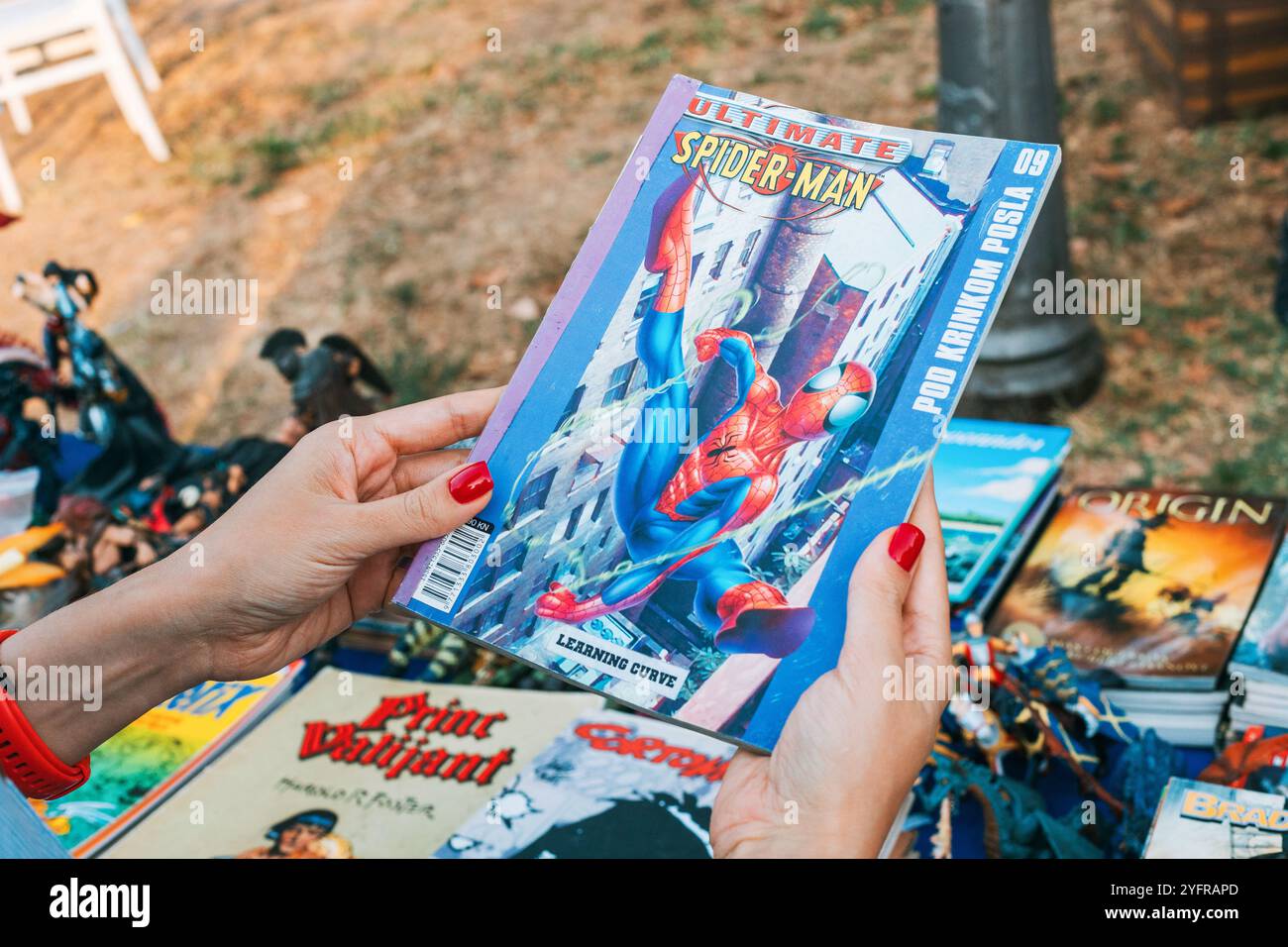 1. September 2024. Belgrad, Serbien: Person mit rot bemalten Nägeln hält einen Comic mit dem Titel Ultimate Spider-man vor dem Hintergrund eines Outdoor-Buches Stockfoto