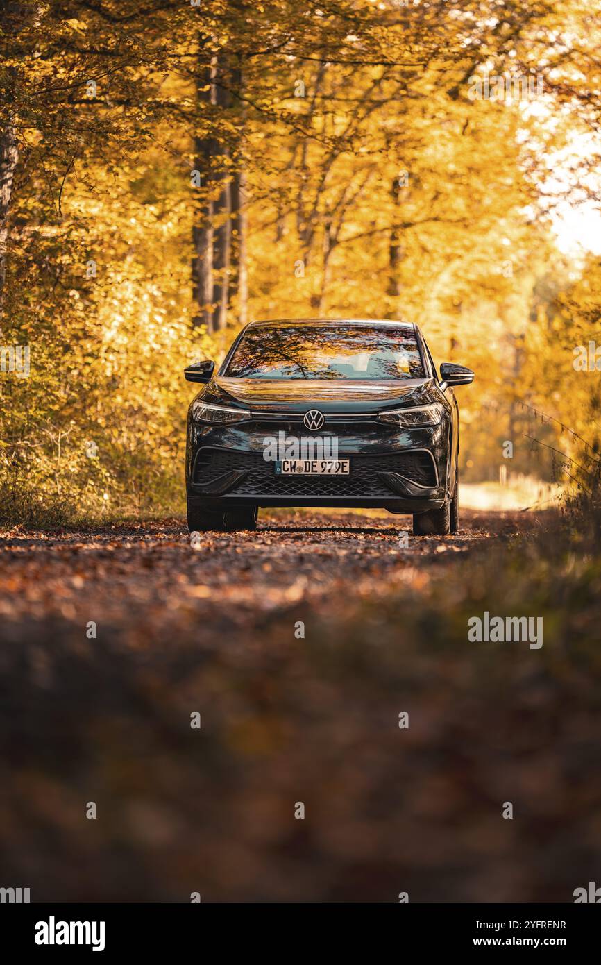 Auto auf einem Herbstweg im Wald, eingetaucht in goldene Blätter und Sonnenlicht, Elektroauto VW ID5, Gechingen, Schwarzwald, Deutschland, Europa Stockfoto