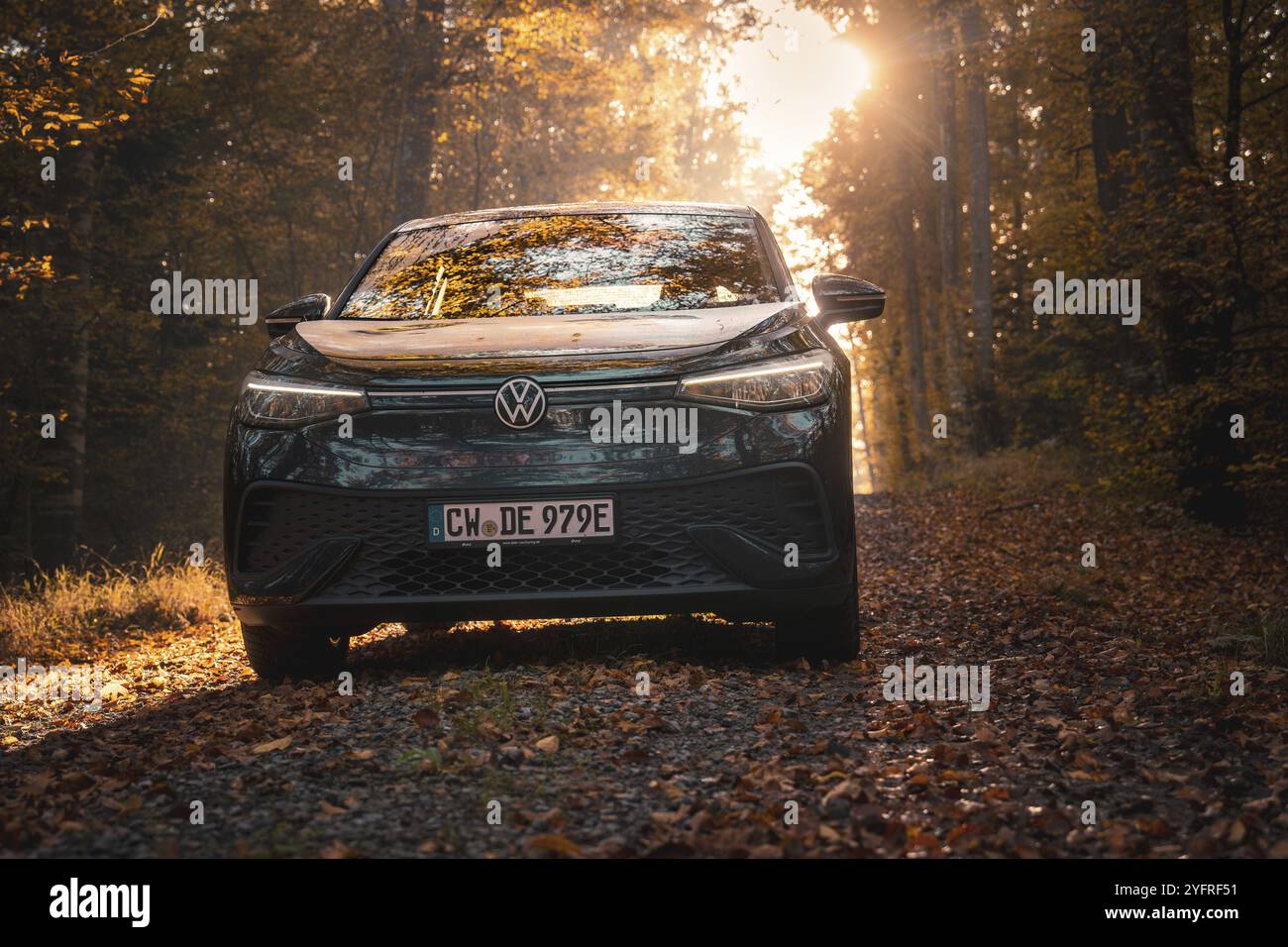Auto im goldenen Licht der Abendsonne auf einem herbstlichen Waldweg mit Blättern, Elektroauto VW ID5, Gechingen, Schwarzwald, Deutschland, Europa Stockfoto