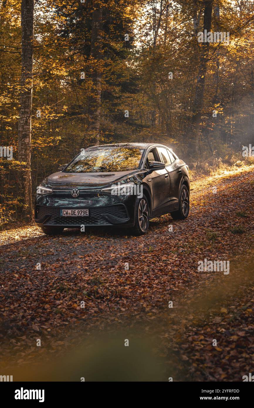 Auto in einem herbstlichen Wald beleuchtet von Sonnenstrahlen, ruhige Atmosphäre, Elektroauto VW ID5, Gechingen, Schwarzwald, Deutschland, Europa Stockfoto