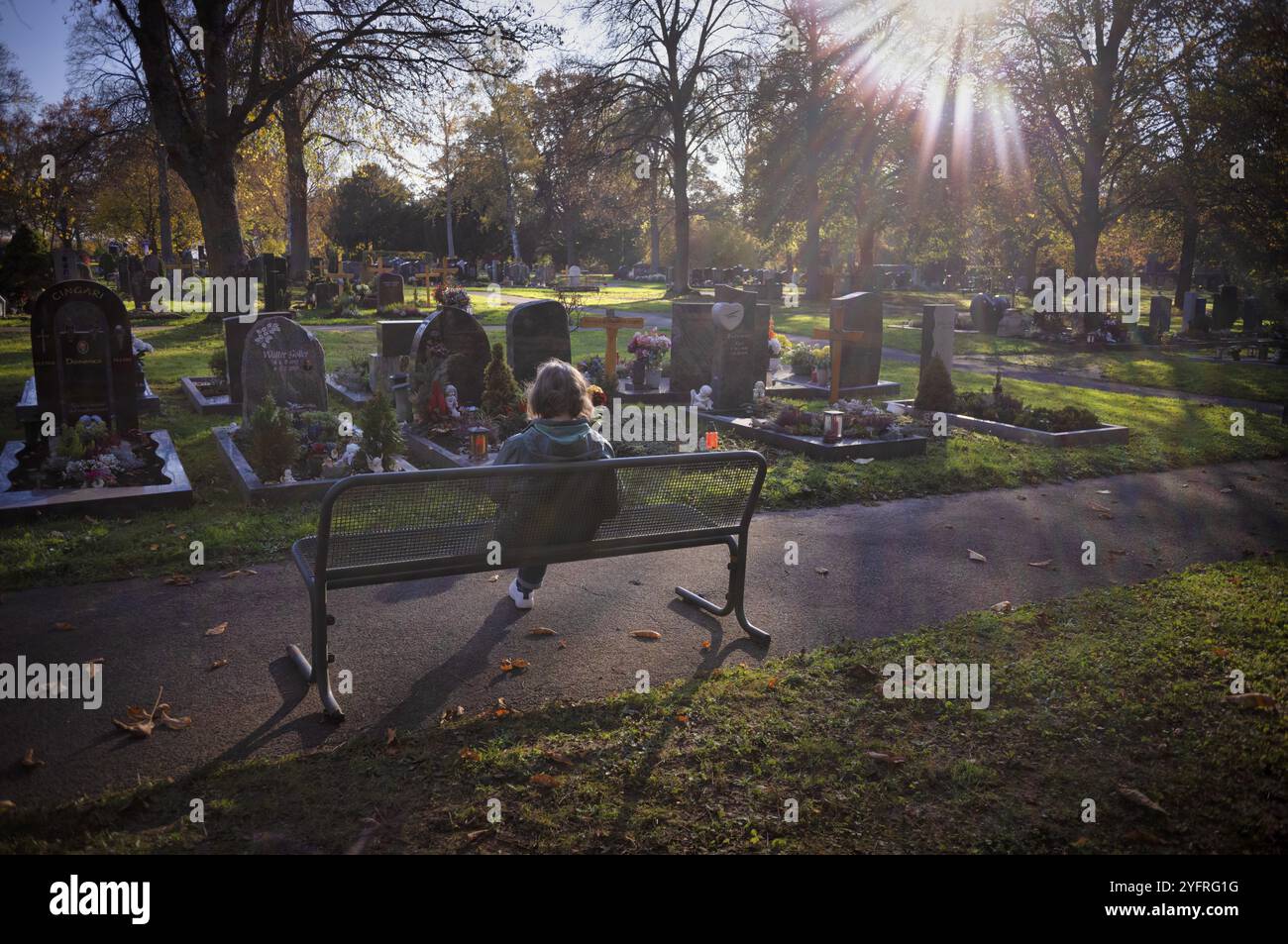 Ältere Frau, die auf der Bank sitzt, auf Grab, Gräber, Tauer, Einsamkeit, Herbstfarben, Herbst, Hintergrundbeleuchtung, Hauptfriedhof, Stuttgart, Baden-Wuertt Stockfoto