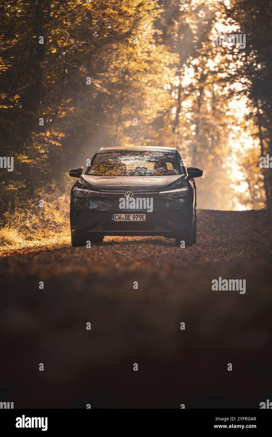 Auto auf einem herbstlichen Waldweg, umgeben von goldenen Blättern und hellem Sonnenlicht, Elektroauto VW ID5, Gechingen, Schwarzwald, Deutschland, Europa Stockfoto