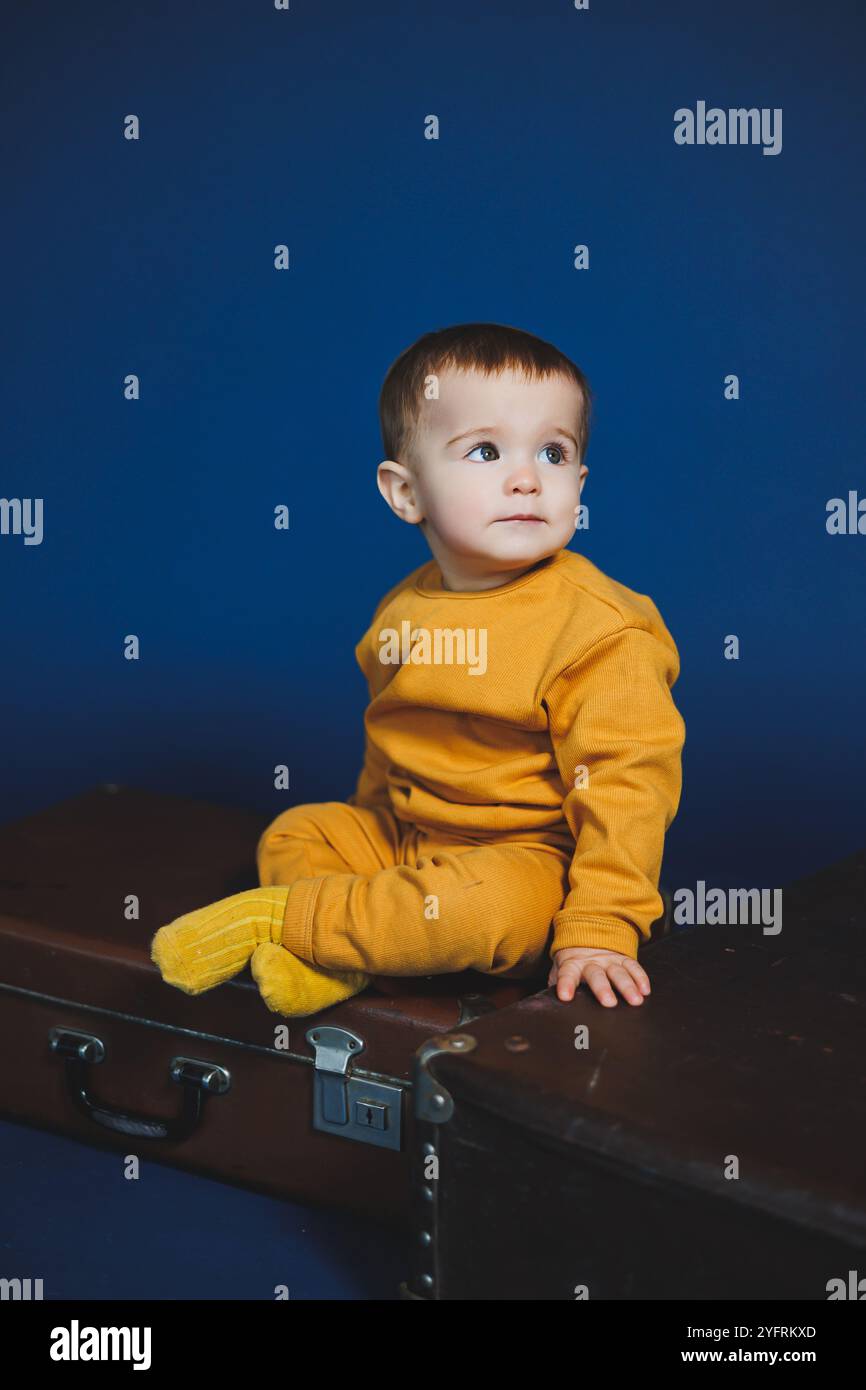 Ein kleiner Junge von 1 Jahr in einem gelben Strickanzug auf blauem Hintergrund. Alltagsgegenstände für Kinder. Stockfoto