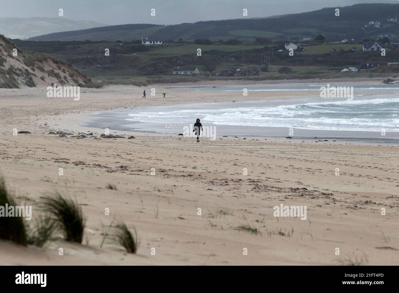 Die Sanddünen liegen im Hinterkopf und die Menschen laufen entlang der fünf-Finger-Strande, der Halbinsel inishowen, der Grafschaft donegal, der republik irland Stockfoto