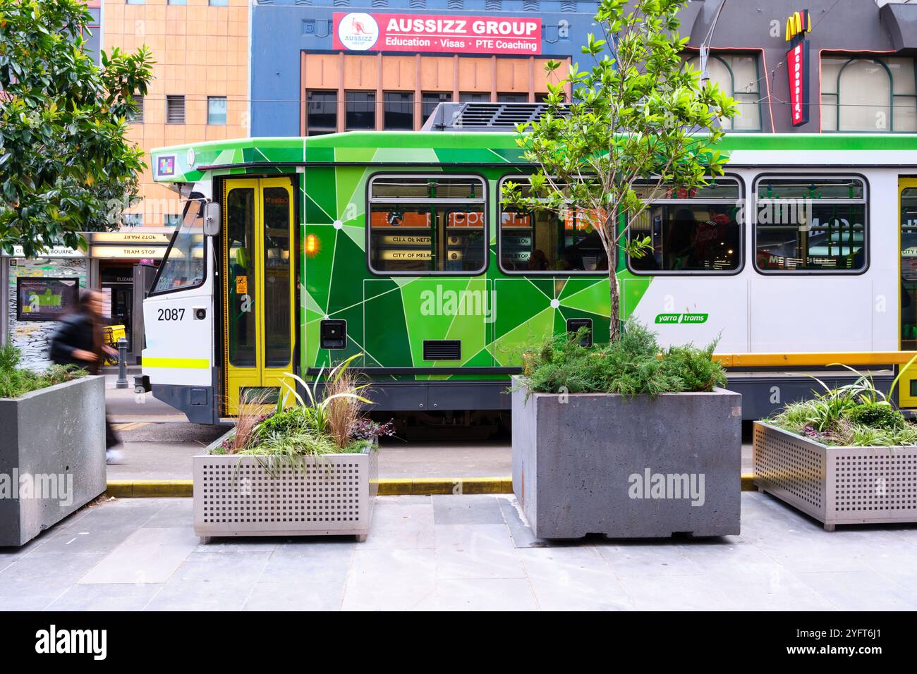 Pflanzen in Pflanzkästen sorgen für städtisches Grün vor einer Straßenbahn in Melbourne an einer Straßenbahnhaltestelle in Elizabeth Street, Melbourne CBD, Victoria, Australien. Stockfoto