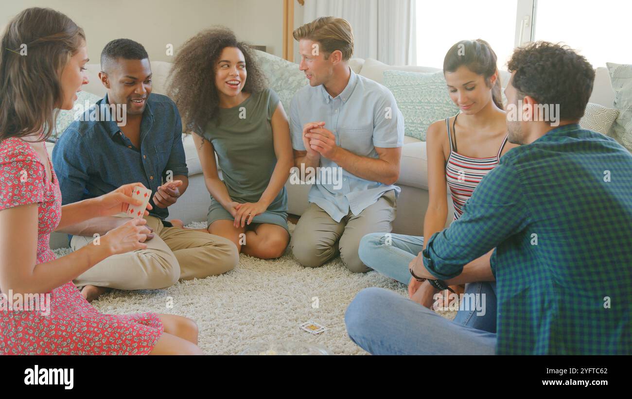 Gruppe Junger Freunde, Die Zu Hause Auf Dem Boden Sitzen Und Gemeinsam Karten Spielen Stockfoto