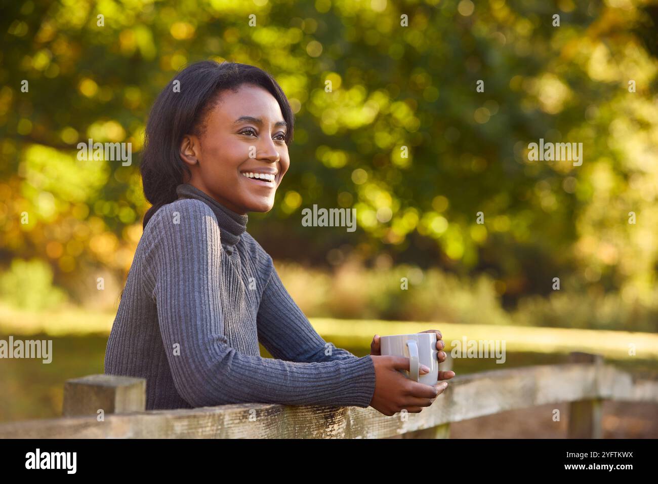 Profil Ansicht Der Jungen Frau Auf Einem Spaziergang In Der Herbstlichen Landschaft, Die Sich Auf Einen Zaun Mit Einem Heißgetränk Stützt Stockfoto