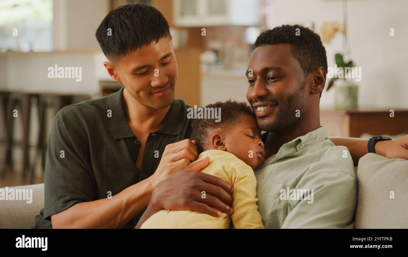 Zwei Väter umarmen ihr schlafendes Baby bequem zu Hause. Stockfoto