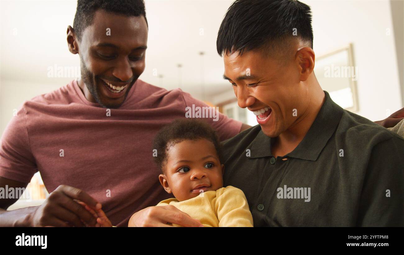 Zwei Männer interagieren glücklich mit ihrem Baby in einem hellen, einladenden Zuhause. Stockfoto