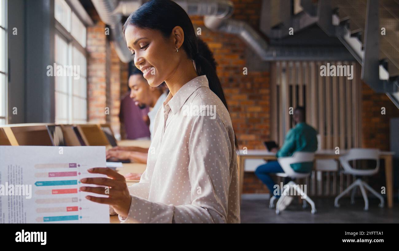 Geschäftsfrau Mit Laptop, Die In Einem Modernen Multikulturellen Großraumbüro Arbeitet Und Dokumente Ansieht Stockfoto