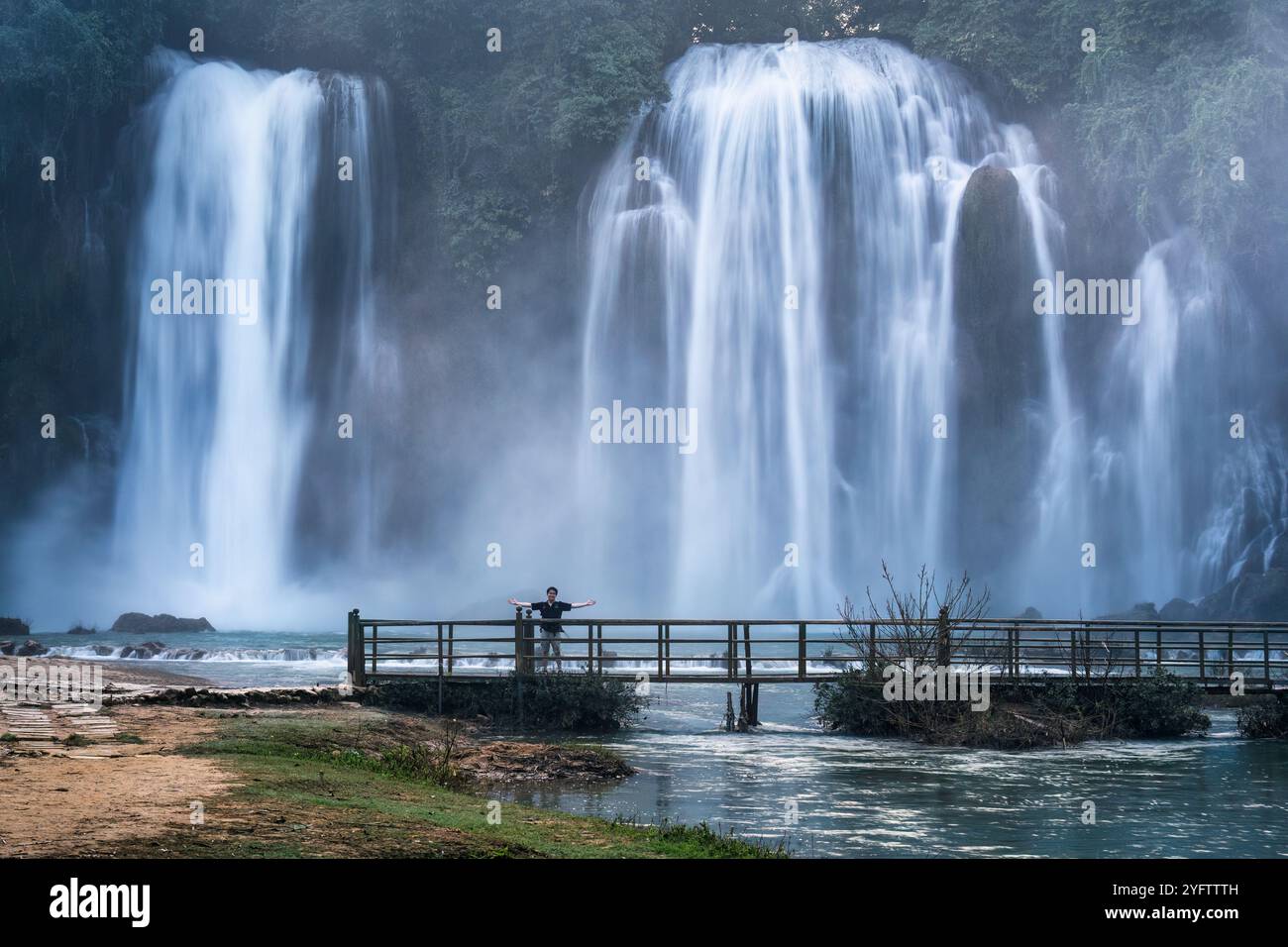 Majestätischer Ban Gioc Wasserfall fließende Bewegung mit männlichen Touristen, die auf einer Holzbrücke in Cao Bang, Vietnam, stehen Stockfoto