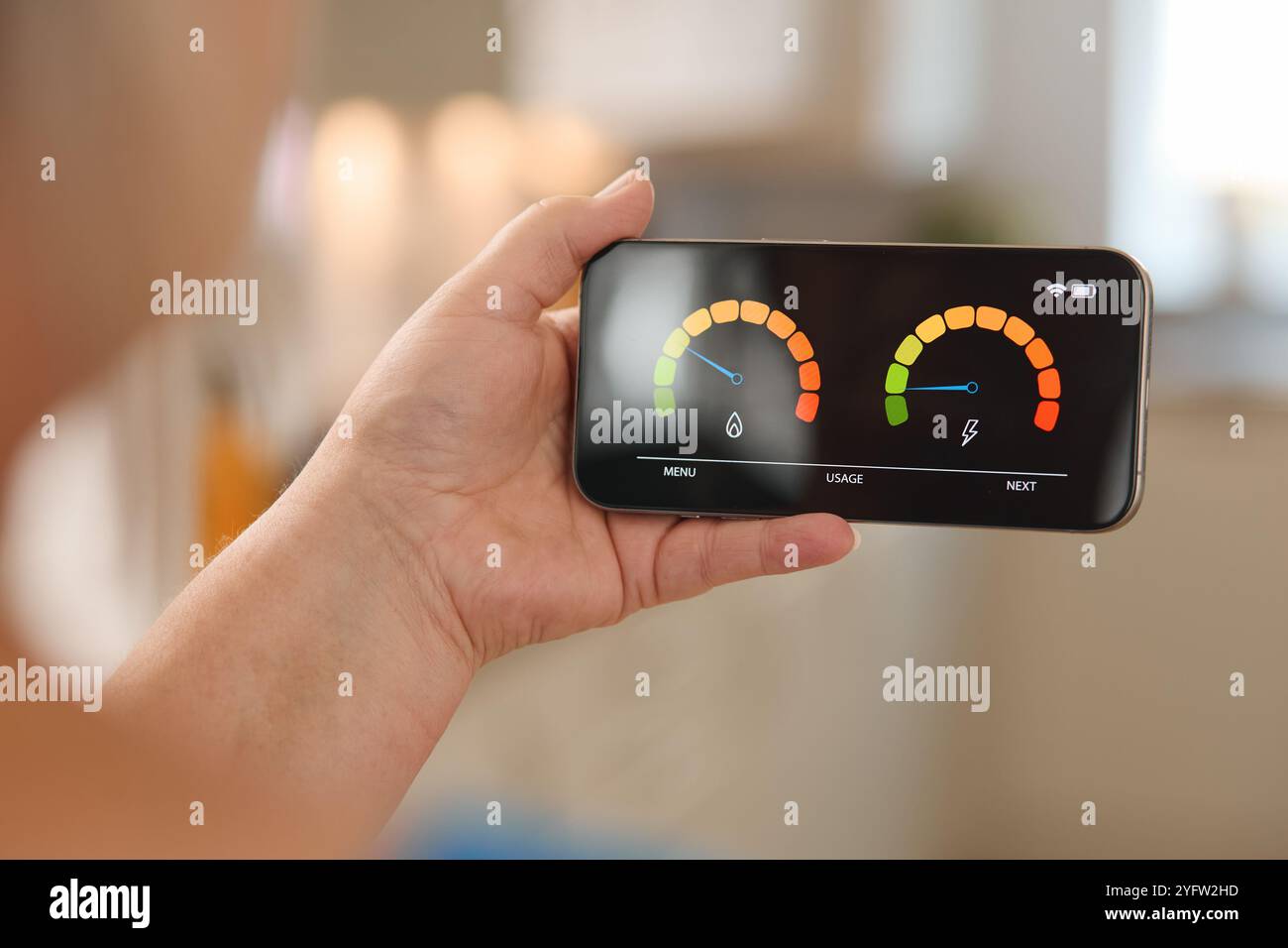Eine Person untersucht ein Smartphone, das einen Energieverbrauchszähler mit bunten Anzeigen anzeigt. Die Umgebung ist hell und modern, was einen andeutet Stockfoto