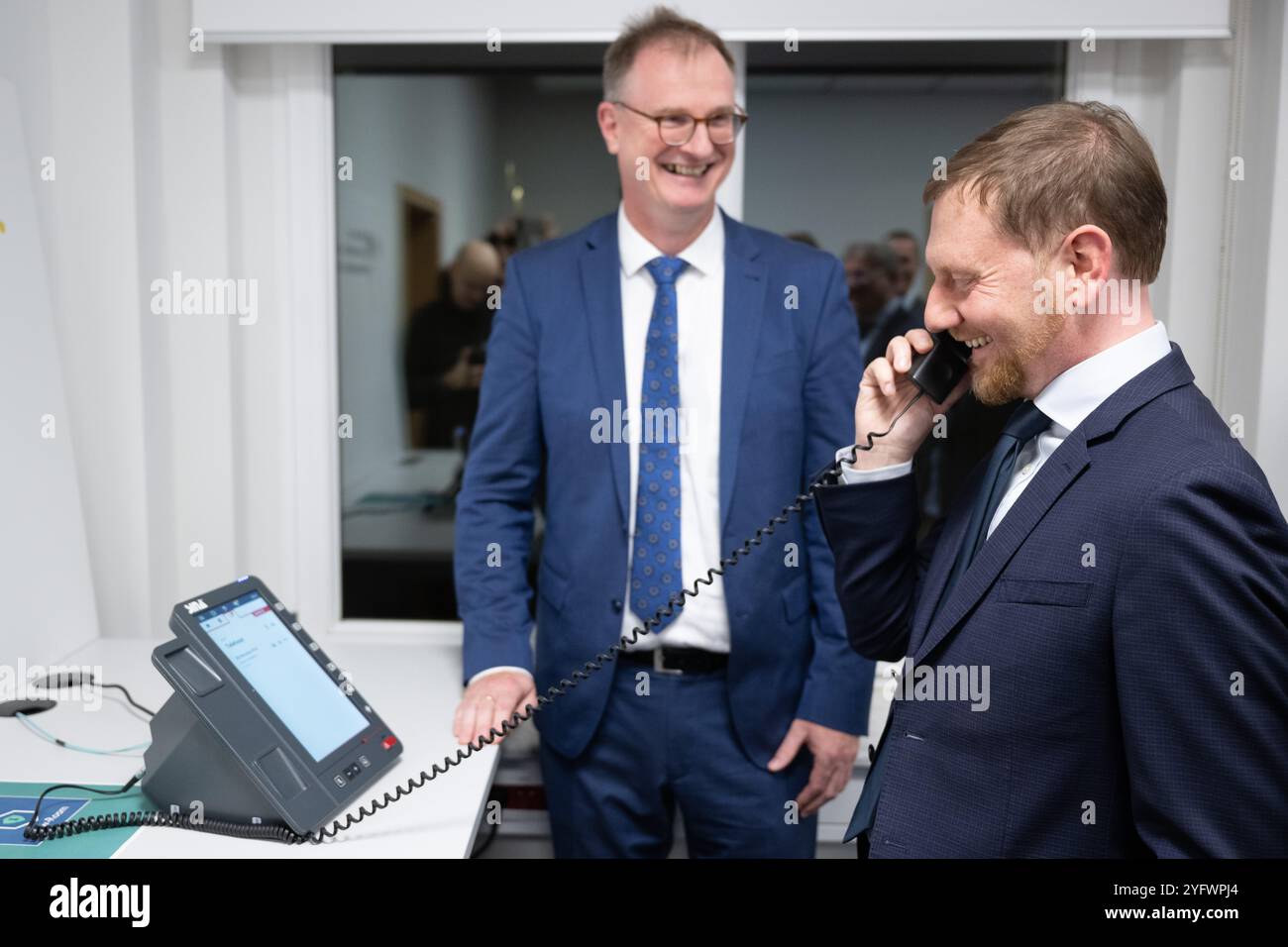 Freital, Deutschland. November 2024. Günther Welsch (l), Leiter der Abteilung Kryptotechnologie, erklärt dem sächsischen Ministerpräsidenten Michael Kretschmer (CDU) ein Telefon für die Hochsicherheits-Telefonielösung zur Übermittlung von Verschlusssachen beim Bundesamt für Sicherheit in der Informationstechnik (BSI). Die Telefonielösung ist für den Testbetrieb in Sachsen vorgesehen. Quelle: Sebastian Kahnert/dpa/Alamy Live News Stockfoto