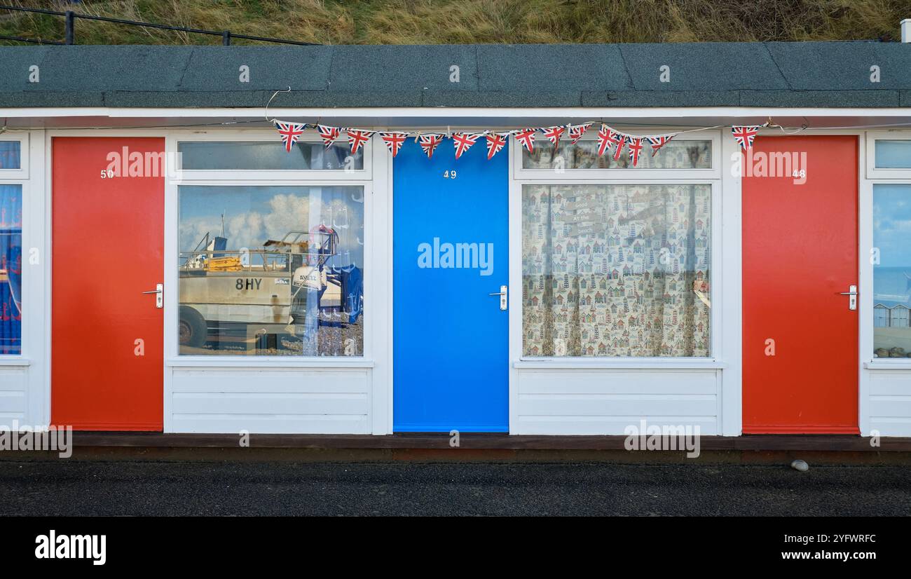 Strandchalets mit weißen und blauen Türen. Farbenfrohe Chalets am Meer in Cromer, Norfolk, einem beliebten englischen Ferienort. Reflexionen in Fenstern. Stockfoto