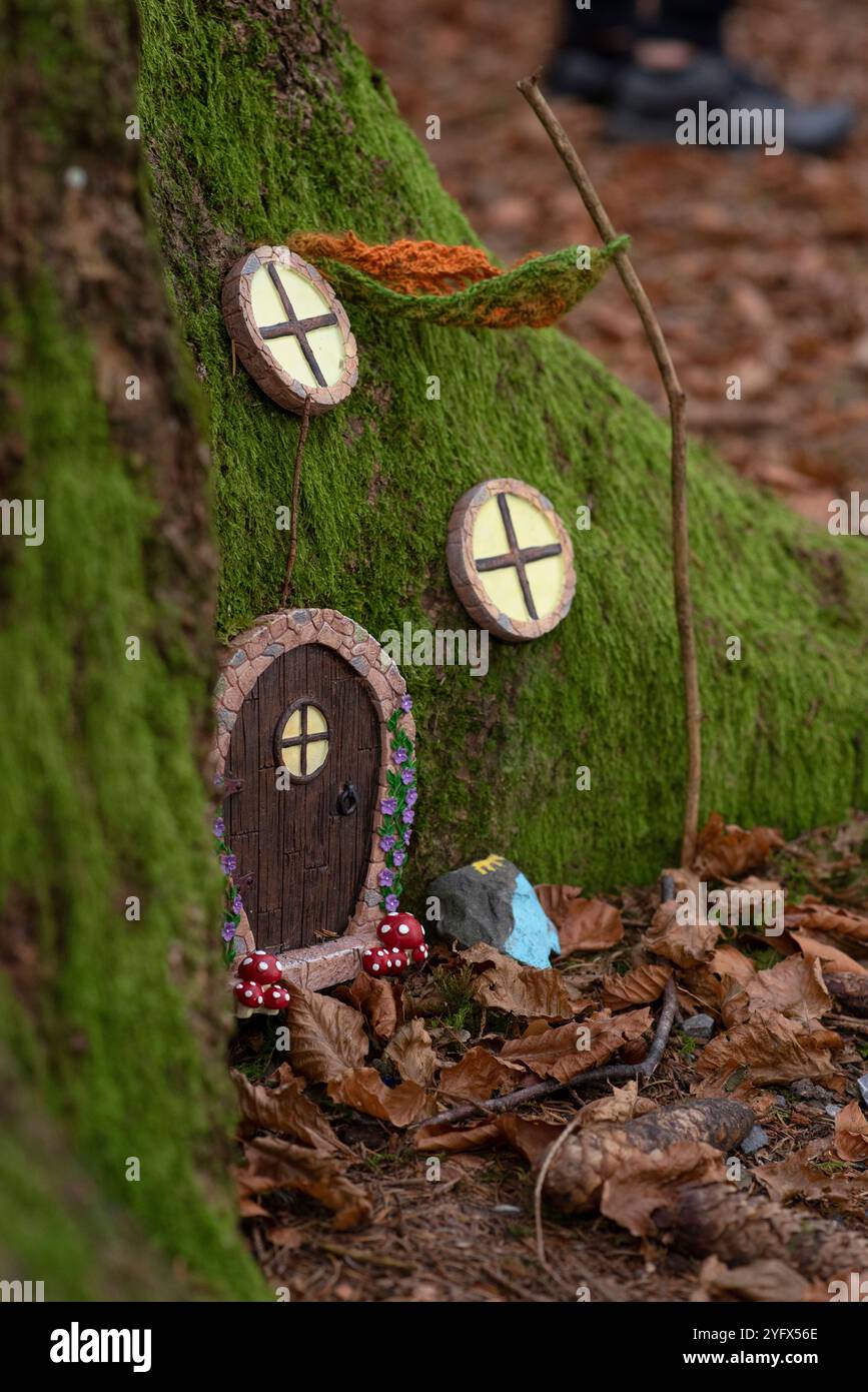Ein Nahfoto einer bezaubernden Miniatur-Feentür an einem moosbedeckten Baumstamm, tief in einem Herbstwald. Umgeben von Gefallenen Stockfoto
